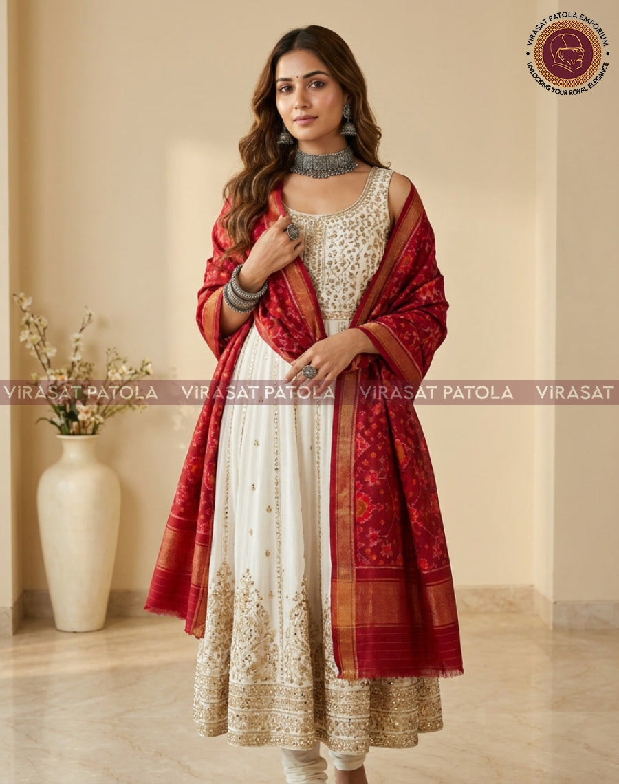 Red patola shawl worn over a cream dress, draped with gold border and decorative motifs