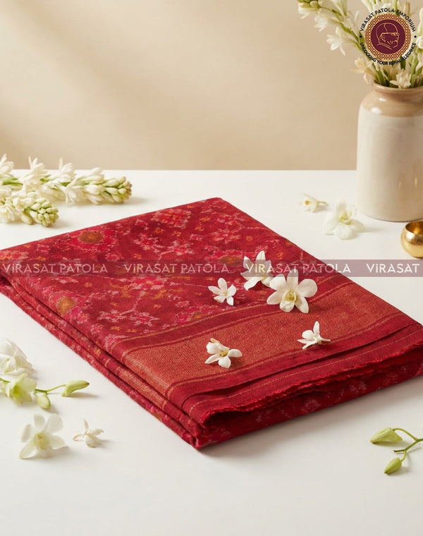 Red patola shawl folded on table, patterned weave with gold-toned details and motifs