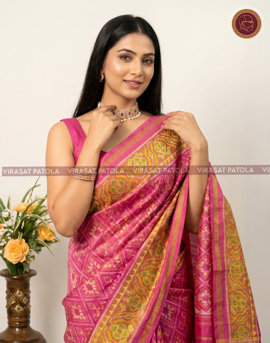 Pink patola saree close-up drape with golden-green woven motifs and striped border