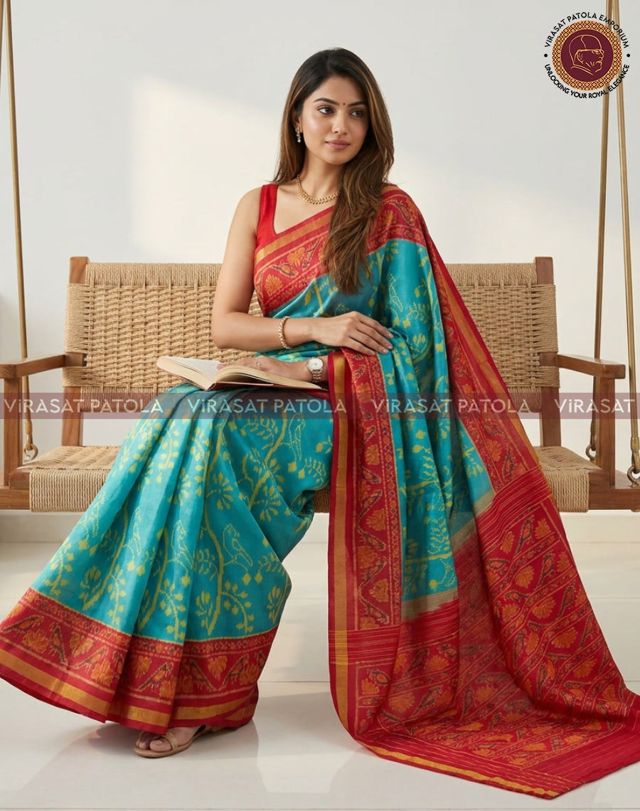 Turquoise patola saree with red patterned border and gold motifs, seated drape